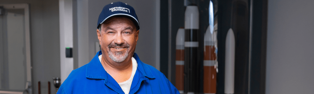 A Latino man in a blue work suit and hat